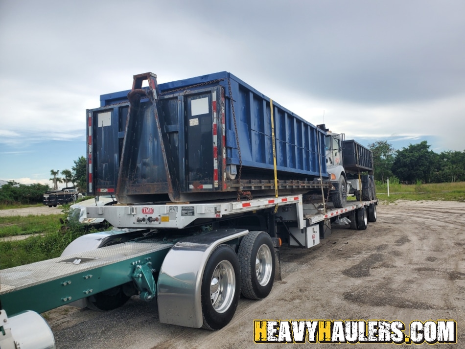 Transporting a blue dump truck on a step deck trailer.