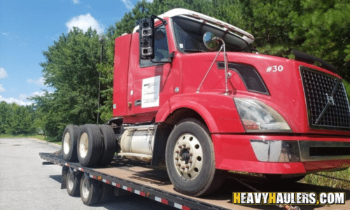Transporting a red Volvo semi truck on a flatbed trailer.