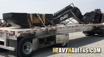 Strapping a Kobelco bucket, boom, and counterweight on a trailer for transport.