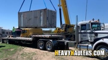 A twenty foot container being loaded on a trailer with a crane.