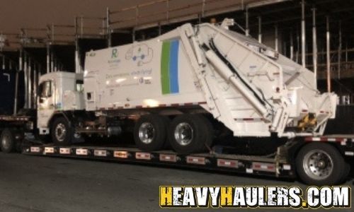 Hauling a garbage truck on a trailer.