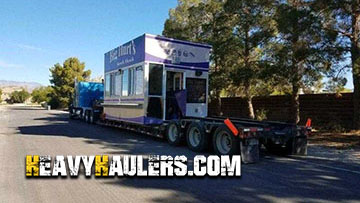 Tiny home converted into a restaurant transported on a lowboy trailer.