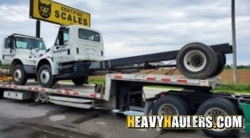 Two semi trucks transported on a step deck trailer.